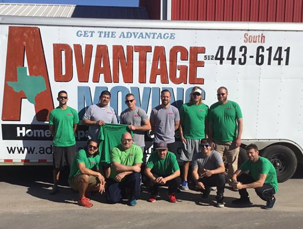 The Advantage Moving crew in green and gray company shirts in front of their branded trailer