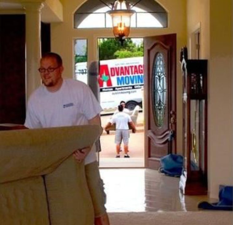 An Advantage mover carrying a sofa through a customer’s entryway, with the company truck outside